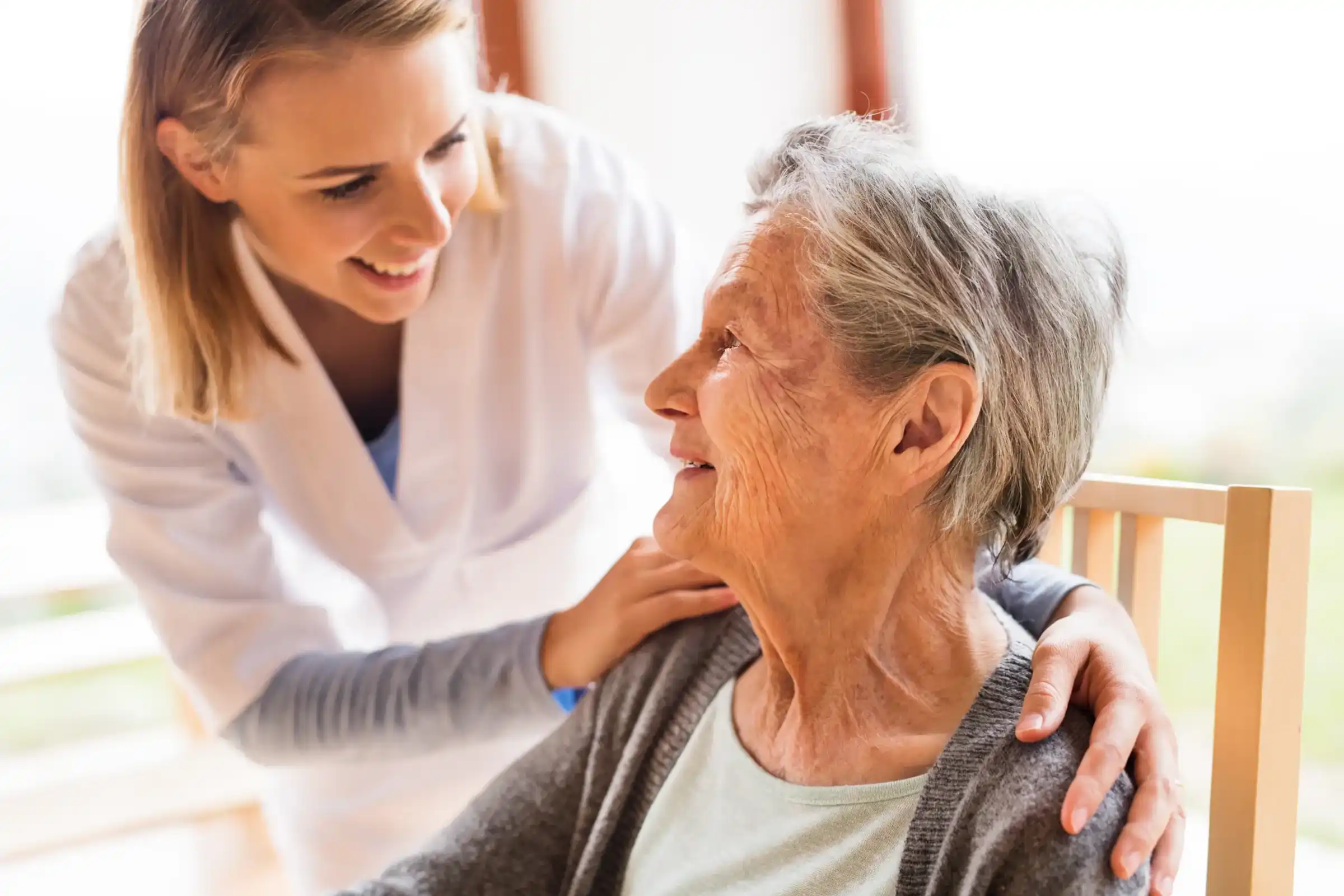 Nurse compassionately holding older woman's shoulders while she is talking to her.