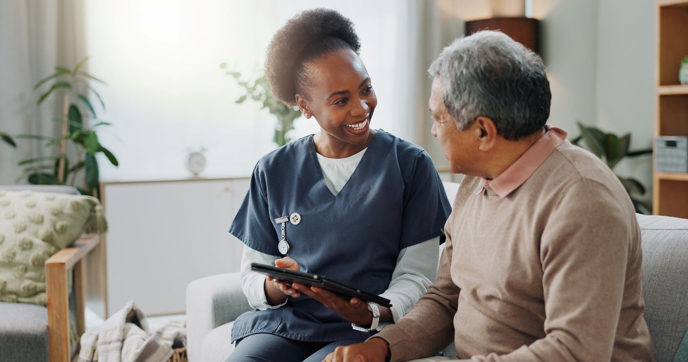 A nurse helps her elderly patient read from a tablet while smiling