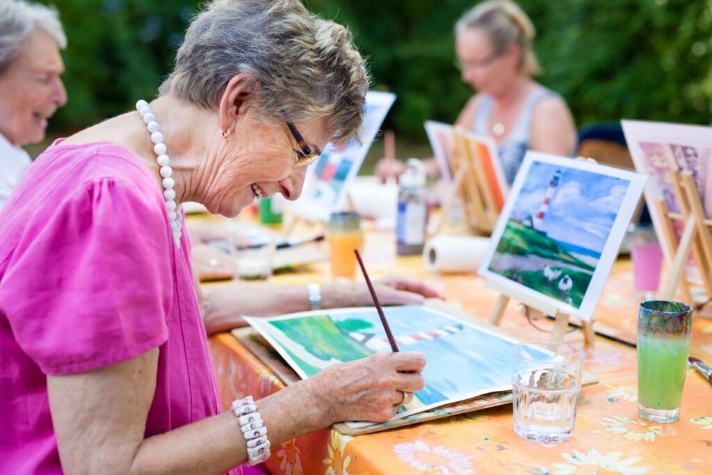 A group of senior women paint lighthouses sitting outdoors.