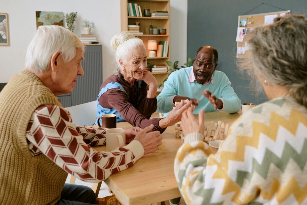 A group of seniors drink coffee and play Jenga around a wooden table. (